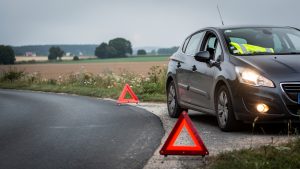 Voiture familiale immobilisée sur le bas-côté d’une route française, avec feux de détresse allumés, gilet réfléchissant visible dans l’habitacle et triangle de signalisation placé à distance.